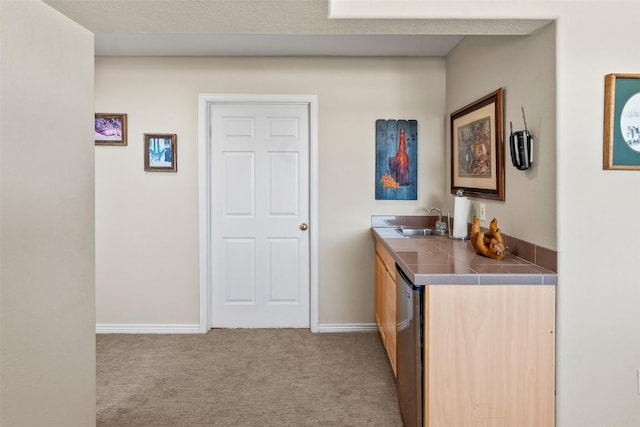 interior space featuring tile countertops, stainless steel dishwasher, a sink, carpet floors, and baseboards