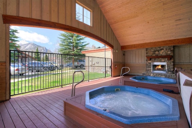 view of pool with hot tub deck surround, an outdoor stone fireplace, and a deck with mountain view