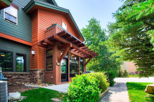 entrance to property featuring cooling unit, stone siding, and a balcony