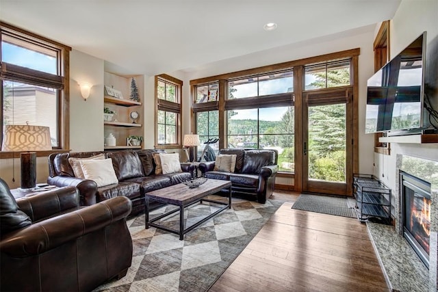 living room with hardwood / wood-style flooring, a high end fireplace, built in features, and recessed lighting
