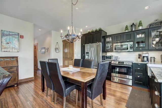 dining area featuring light wood-type flooring, baseboards, recessed lighting, and a notable chandelier