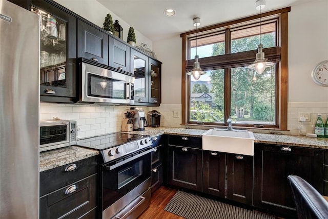 kitchen with stainless steel appliances, a toaster, a sink, glass insert cabinets, and light stone countertops