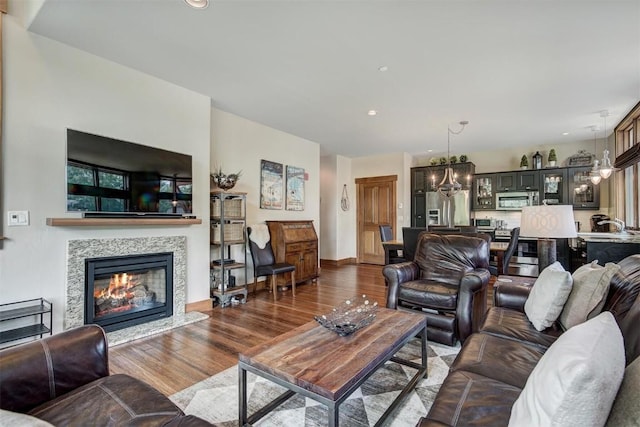 living area with wood finished floors, a glass covered fireplace, an inviting chandelier, baseboards, and recessed lighting