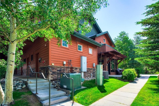 view of home's exterior with a yard, stone siding, and cooling unit