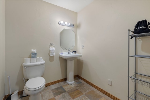 bathroom featuring baseboards, stone finish flooring, and toilet