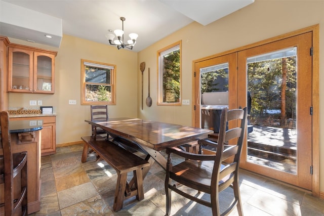 dining room featuring stone finish flooring, a wealth of natural light, a notable chandelier, and baseboards