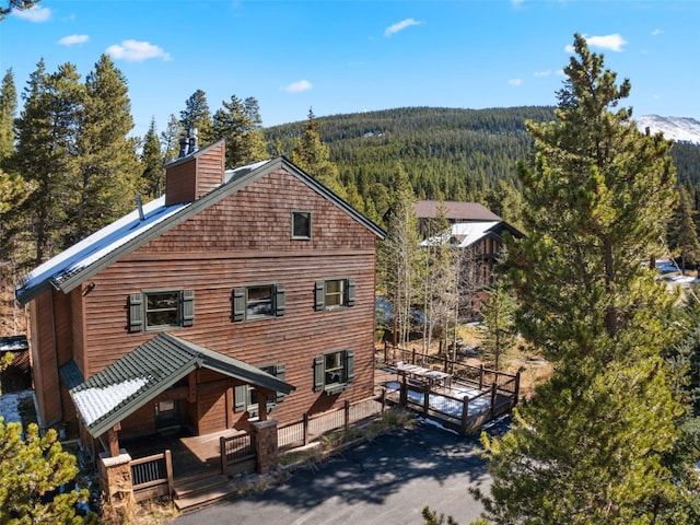 back of property with a chimney, a mountain view, and a wooded view