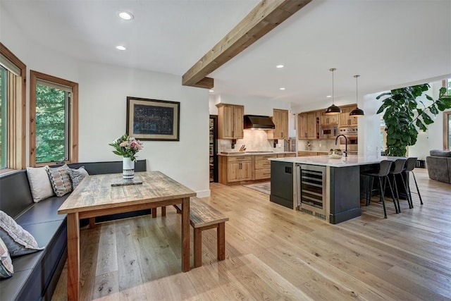 kitchen with extractor fan, beverage cooler, light wood-type flooring, light countertops, and beam ceiling