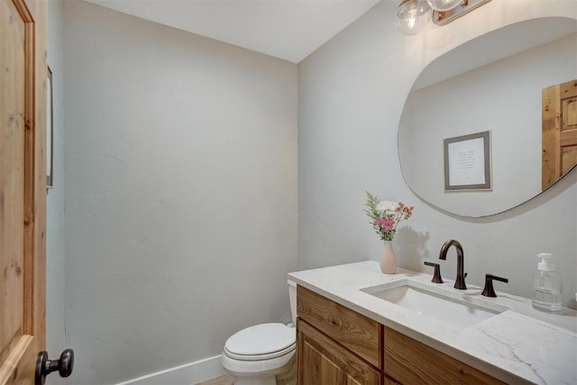 half bathroom with baseboards, vanity, and toilet