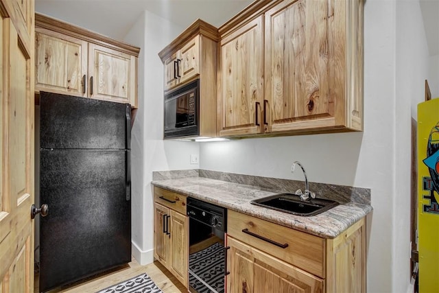 kitchen with black appliances, light stone countertops, a sink, and light wood finished floors