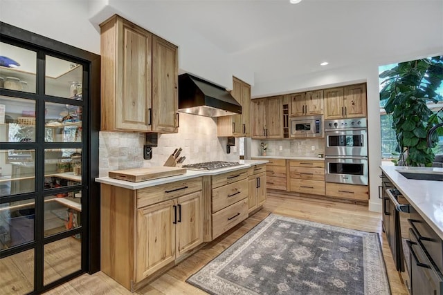 kitchen featuring light countertops, a sink, wall chimney exhaust hood, decorative backsplash, and appliances with stainless steel finishes