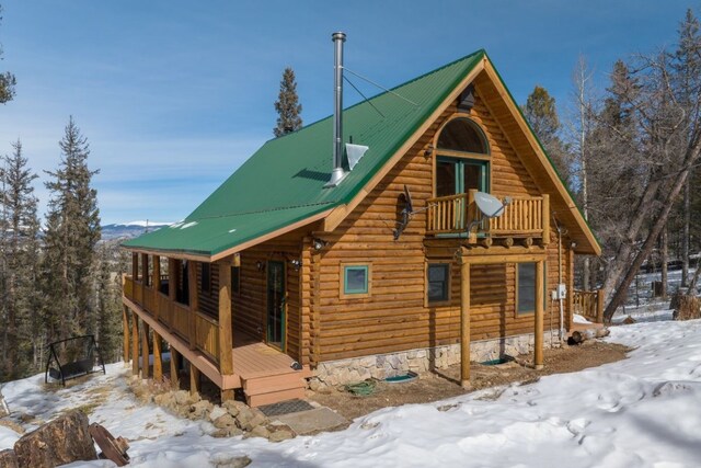 view of snowy exterior featuring log siding, a balcony, and metal roof