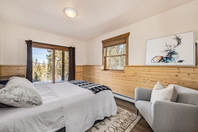 bedroom featuring a baseboard heating unit, wood walls, a wainscoted wall, and wood finished floors