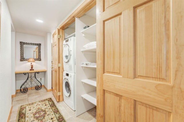 washroom with baseboards, stacked washer / drying machine, tile patterned floors, and laundry area