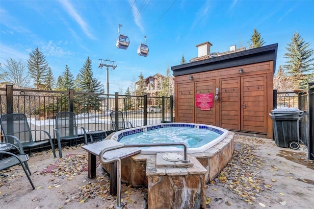 view of pool featuring a storage unit, an outbuilding, an outdoor hot tub, and fence