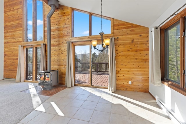 unfurnished dining area featuring a wood stove, wooden walls, a chandelier, tile patterned flooring, and high vaulted ceiling