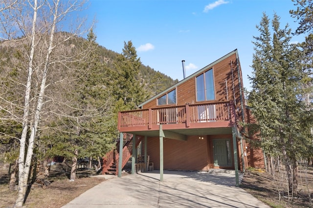 back of house featuring concrete driveway, a deck with mountain view, and stairway