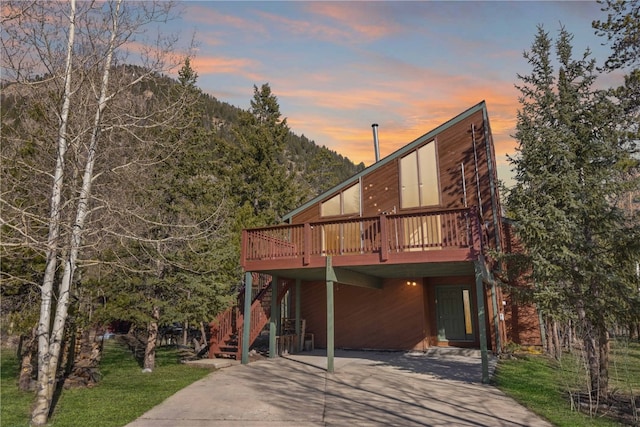 view of front facade with driveway, a wooden deck, a carport, and stairs