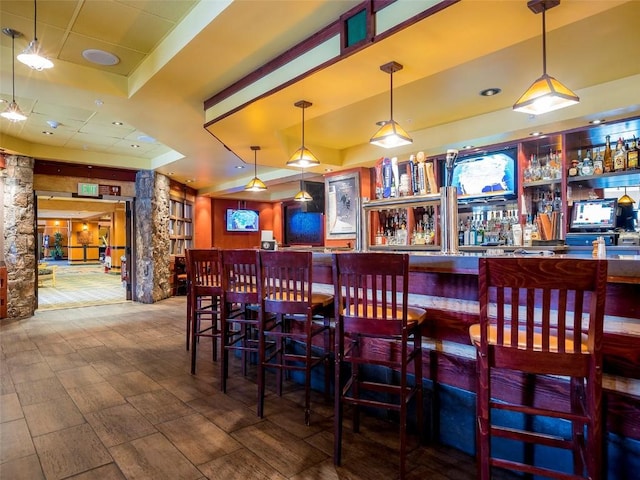 bar with a tray ceiling, hanging light fixtures, and a dry bar