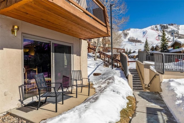 snow covered patio with stairway and a deck with mountain view