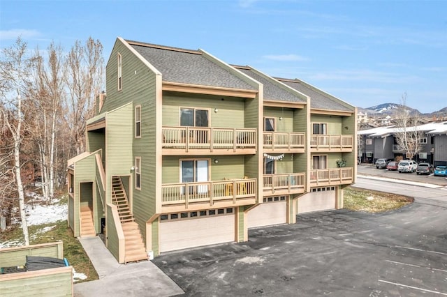 view of front of home with a balcony, driveway, a shingled roof, an attached garage, and a mountain view