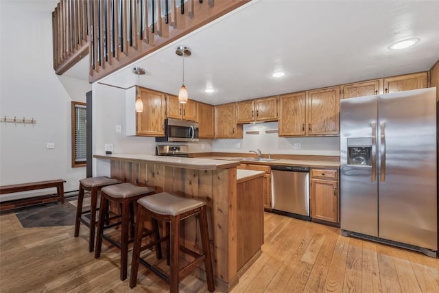 kitchen featuring light wood-style flooring, hanging light fixtures, brown cabinetry, and stainless steel appliances