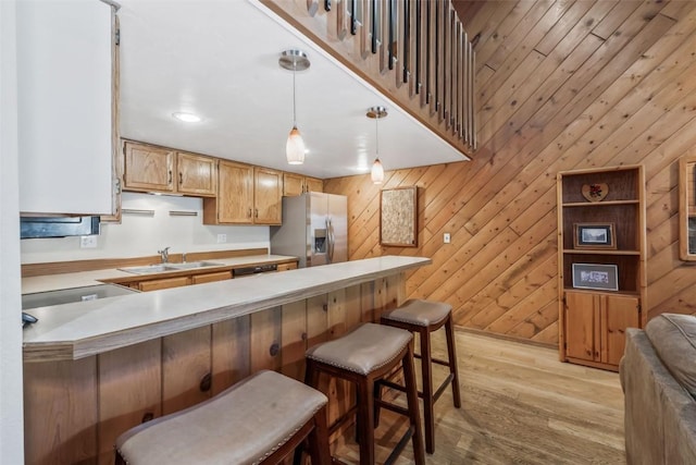 kitchen with light wood finished floors, a peninsula, a sink, stainless steel fridge with ice dispenser, and decorative light fixtures