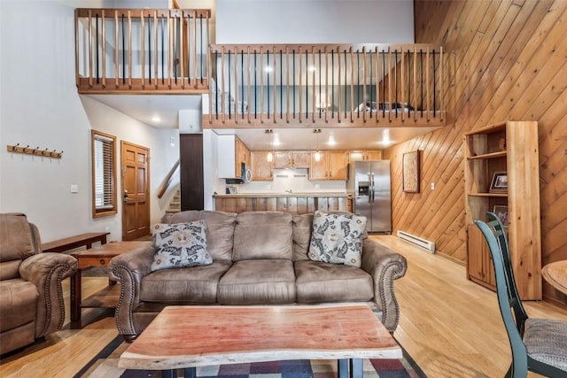 living area with stairway, a towering ceiling, wood walls, light wood-style floors, and baseboard heating