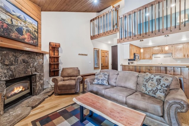 living room featuring wood ceiling, a towering ceiling, a stone fireplace, and wood finished floors