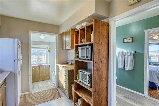 kitchen with stainless steel microwave, freestanding refrigerator, light wood-style floors, open shelves, and light countertops