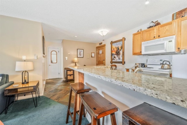 kitchen featuring white microwave, electric range oven, a breakfast bar area, a textured ceiling, and decorative backsplash