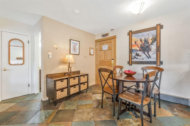 dining area featuring stone tile flooring, a textured ceiling, and baseboards