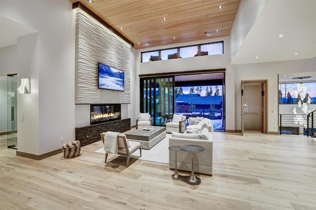 living room with light hardwood / wood-style floors, wooden ceiling, a fireplace, and a towering ceiling