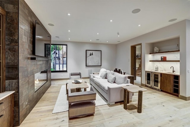 living room featuring a multi sided fireplace, light wood-type flooring, beverage cooler, and sink