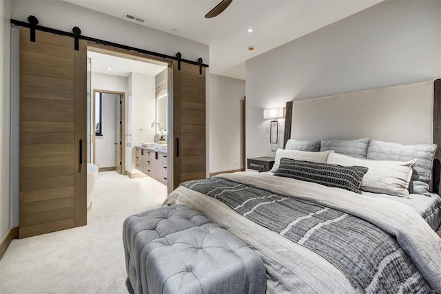 bedroom with ensuite bathroom, a barn door, light colored carpet, and ceiling fan