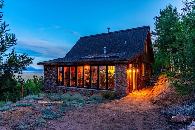 1023 Raven Way, Como, CO 80432 - back of house at dusk featuring solar panels, roof with shingles, and stone siding