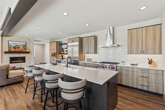 kitchen featuring a breakfast bar, a sink, modern cabinets, wall chimney exhaust hood, and built in appliances