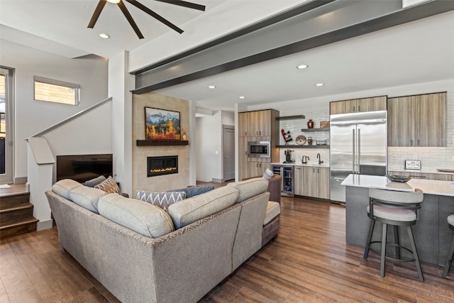 living area with stairway, dark wood-style floors, a tiled fireplace, ceiling fan, and bar