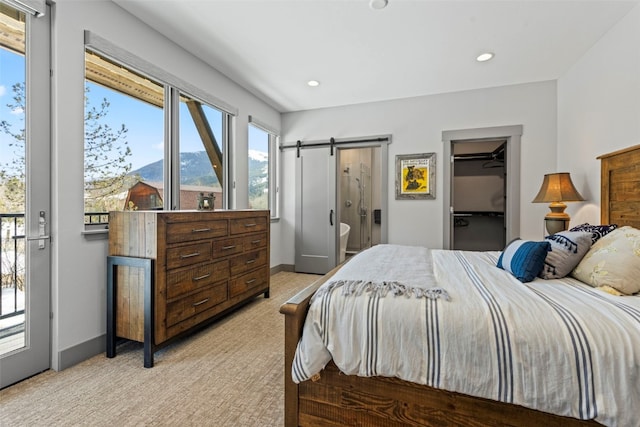 bedroom with a barn door, recessed lighting, a walk in closet, baseboards, and light colored carpet