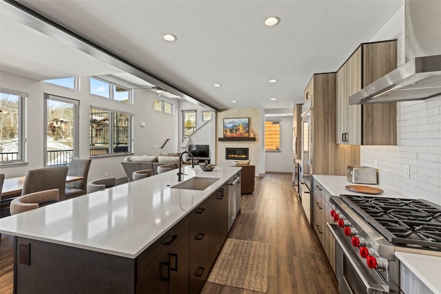 kitchen with wall chimney exhaust hood, stainless steel appliances, a sink, open floor plan, and modern cabinets