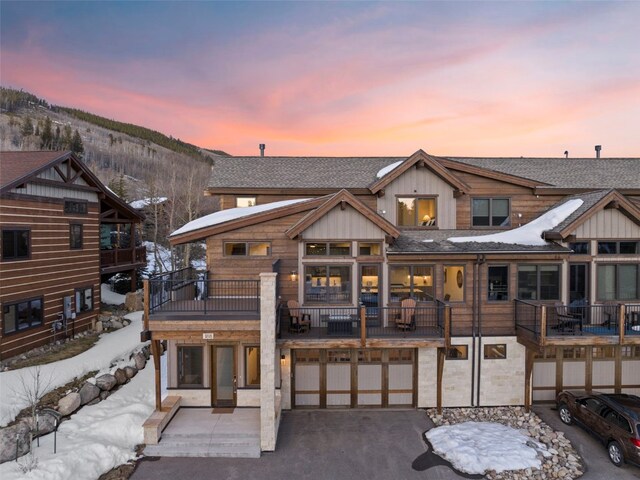 snow covered house with a balcony, aphalt driveway, board and batten siding, a mountain view, and a garage