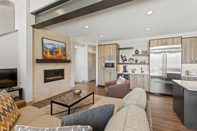 living room with recessed lighting, dark wood-style floors, wine cooler, a tiled fireplace, and indoor wet bar