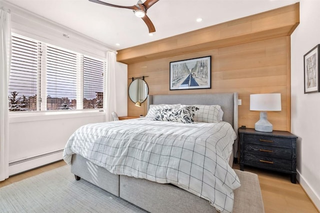 bedroom with a baseboard heating unit, light hardwood / wood-style flooring, wooden walls, and ceiling fan