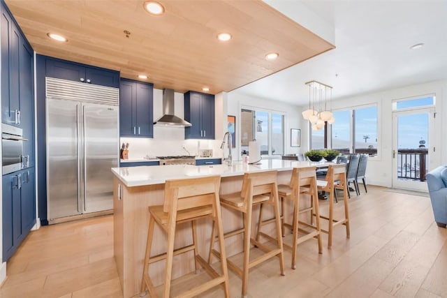 kitchen featuring wall chimney exhaust hood, appliances with stainless steel finishes, a breakfast bar, and a kitchen island with sink