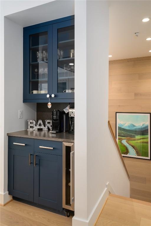 bar featuring blue cabinets, beverage cooler, and light hardwood / wood-style floors