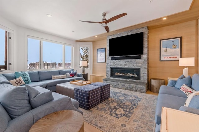 living room with a stone fireplace, ceiling fan, and wood walls