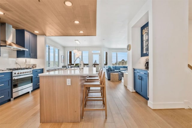 kitchen featuring wood ceiling, a breakfast bar area, a kitchen island with sink, stainless steel range with gas stovetop, and wall chimney exhaust hood