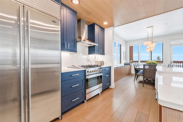 kitchen with wall chimney exhaust hood, decorative light fixtures, blue cabinets, and premium appliances