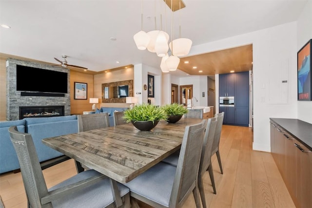 dining area featuring sink, a stone fireplace, light hardwood / wood-style floors, and ceiling fan