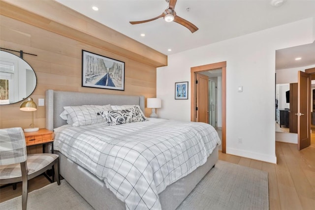 bedroom with ceiling fan, wooden walls, and light hardwood / wood-style floors